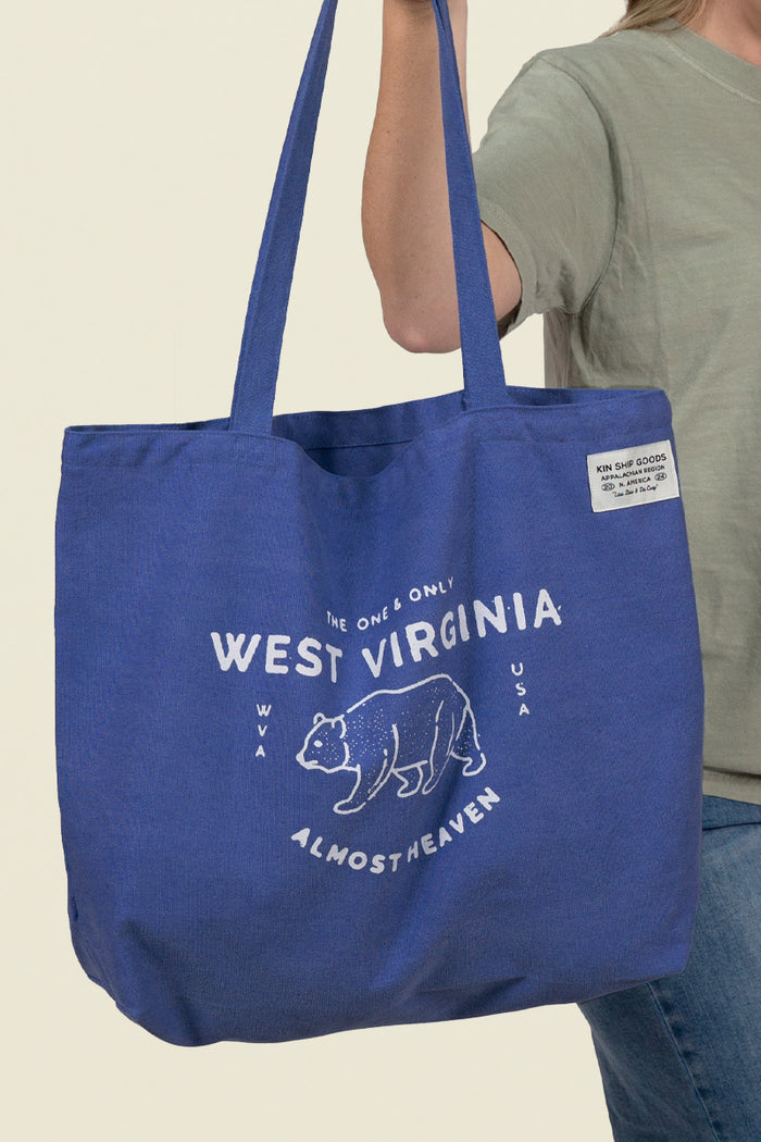 Blue Kin Ship Goods canvas tote with white bear graphic and ‘West Virginia Almost Heaven’ text, laid flat on light background.