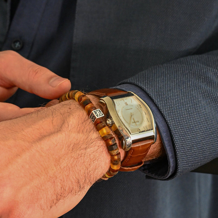 Close-up of a person wearing a gold watch and amberbracelet on a dark suit background
