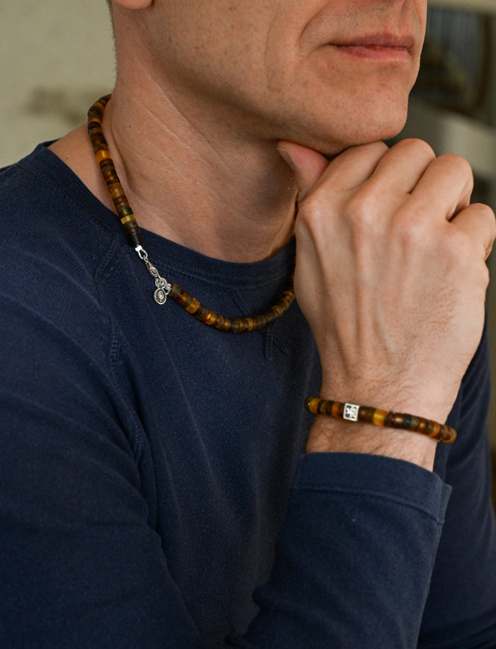 Man wearing a necklace and bracelet with a blurred background