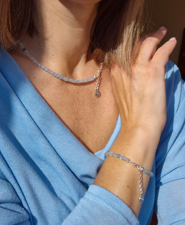 A beaded necklace with light blue aquamarine stones and a handmade silver medallion with a spiral design.