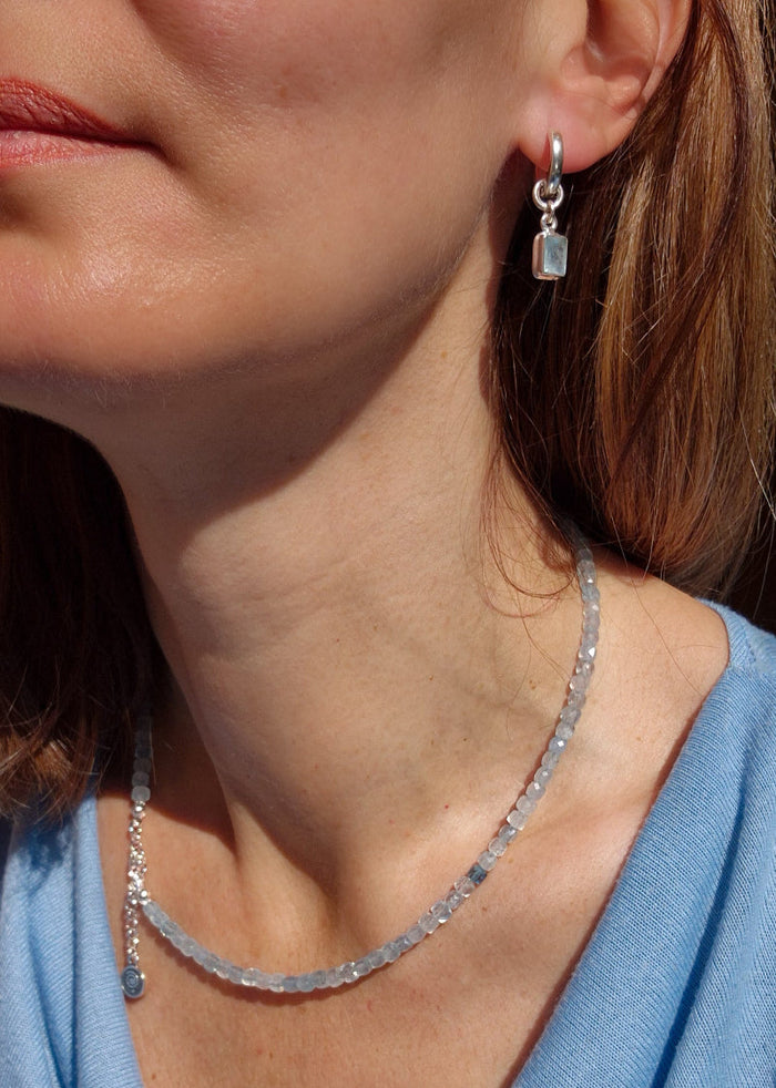 A beaded necklace with light blue aquamarine stones and a handmade silver medallion with a spiral design.top.