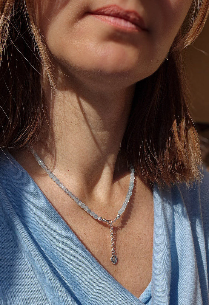 A beaded necklace with light blue aquamarine stones and a handmade silver medallion with a spiral design.