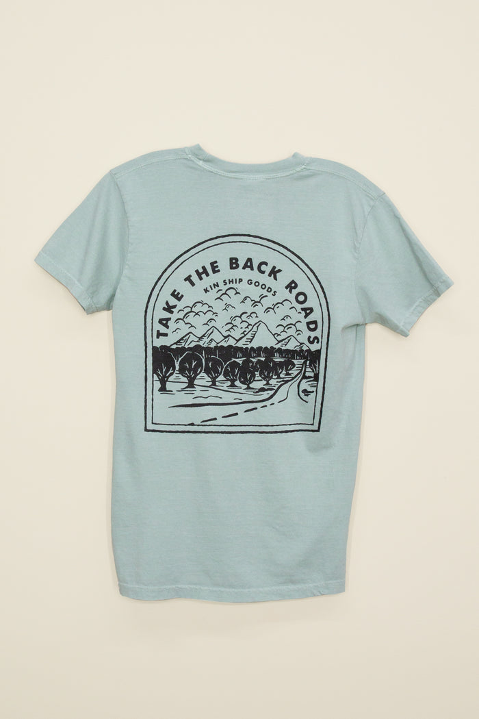 Kin Ship Goods light blue/green pocket tee with ‘Take the Back Roads’ mountain and orchard graphic on back, perfect for slow travel and scenic drives.