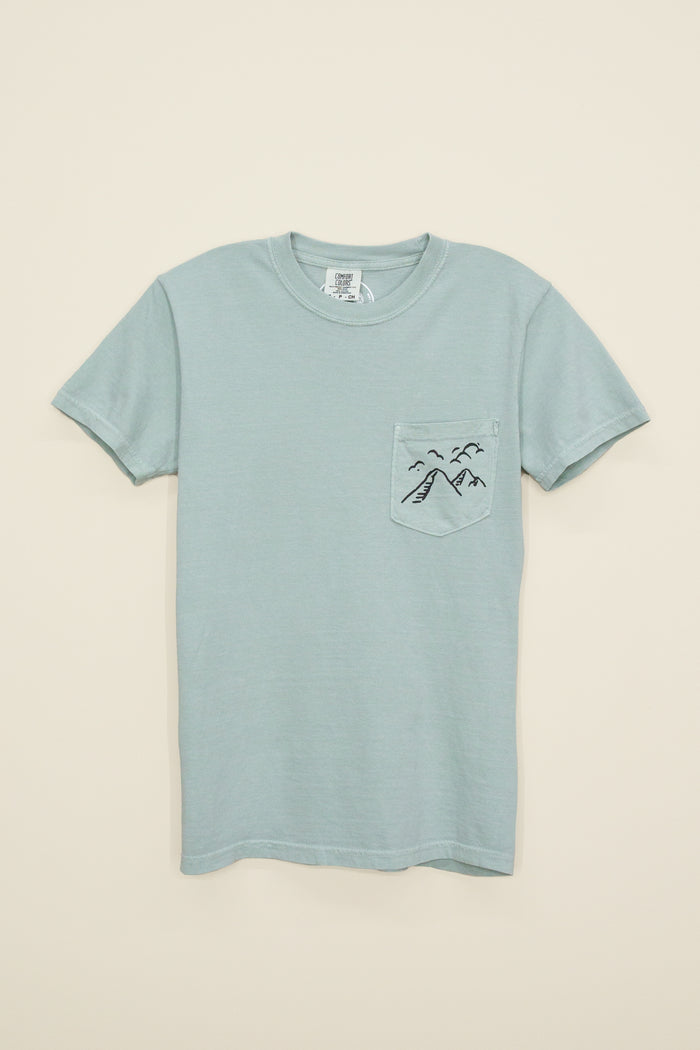 Kin Ship Goods light blue/green pocket tee with ‘Take the Back Roads’ mountain and orchard graphic on back, perfect for slow travel and scenic drives.