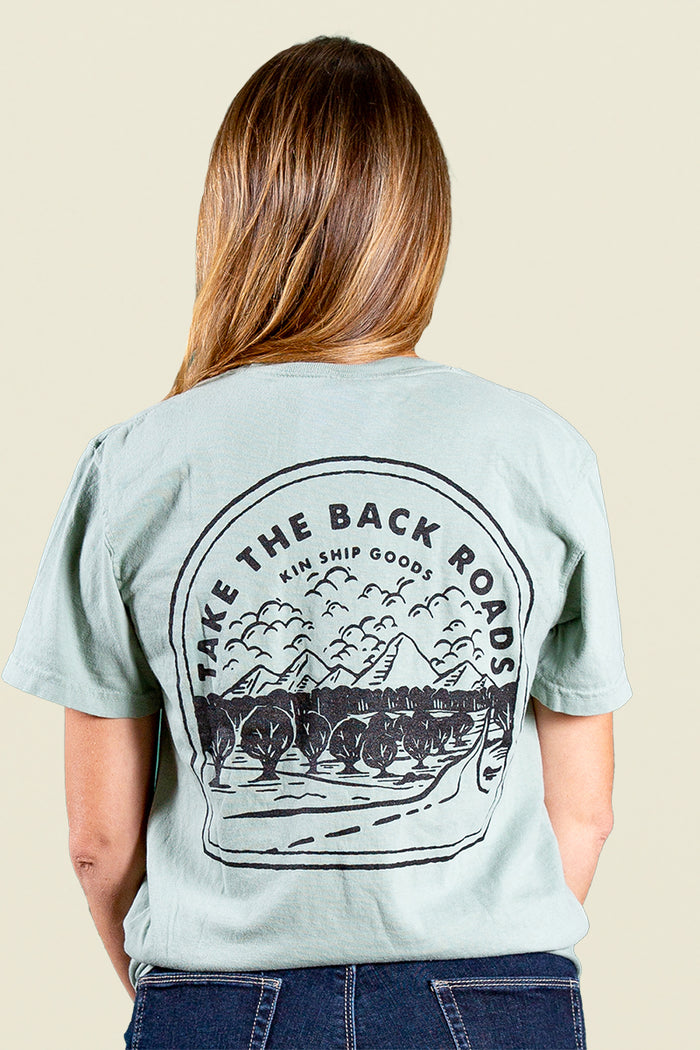 Kin Ship Goods light blue/green pocket tee with ‘Take the Back Roads’ mountain and orchard graphic on back, perfect for slow travel and scenic drives.