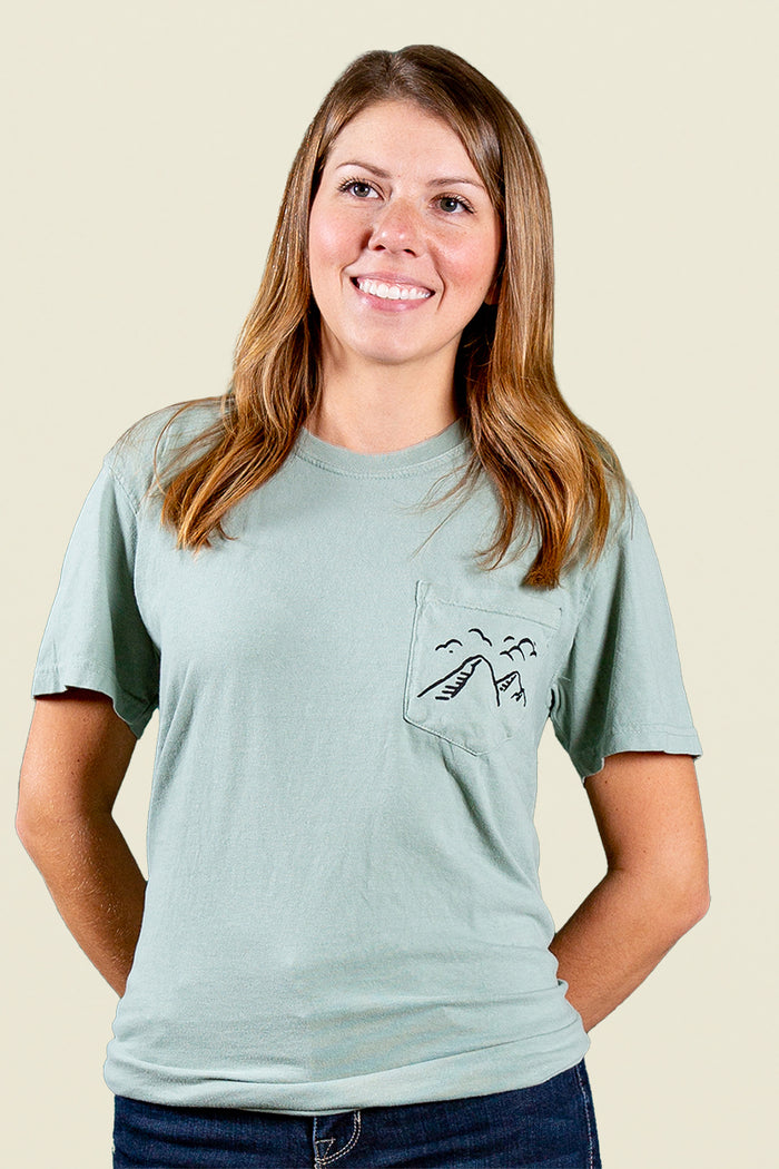 Kin Ship Goods light blue/green pocket tee with ‘Take the Back Roads’ mountain and orchard graphic on back, perfect for slow travel and scenic drives.