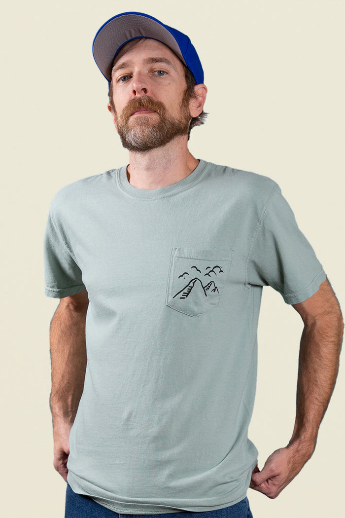 Kin Ship Goods light blue/green pocket tee with ‘Take the Back Roads’ mountain and orchard graphic on back, perfect for slow travel and scenic drives.