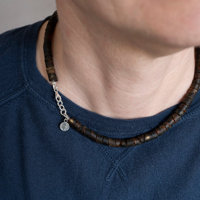 Close-up of a person wearing a dark blue shirt with a Baltic amber necklace featuring wooden beads and a silver chain.