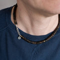 Close-up of a person wearing a dark blue shirt with a Baltic amber necklace featuring wooden beads and a silver chain.