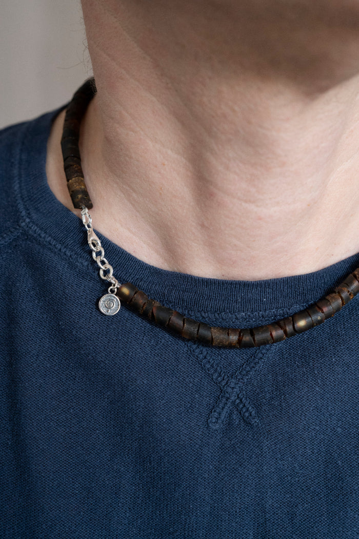Person wearing a dark amber  beaded necklace with a blue shirt
