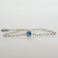 A silver bracelet featuring a faceted cube-shaped kyanite bead and a medallion made of 925 silver, on a white background.