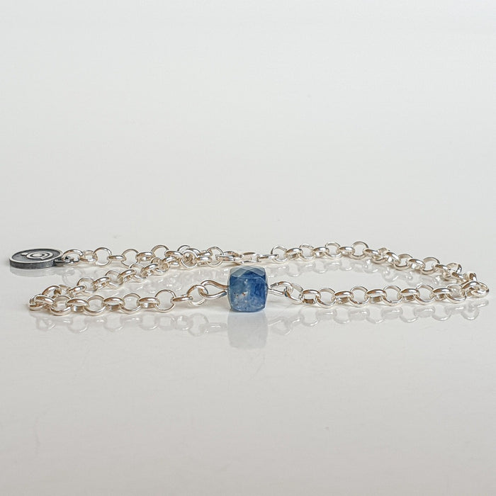 A silver bracelet featuring a faceted cube-shaped kyanite bead and a medallion made of 925 silver, on a white background.