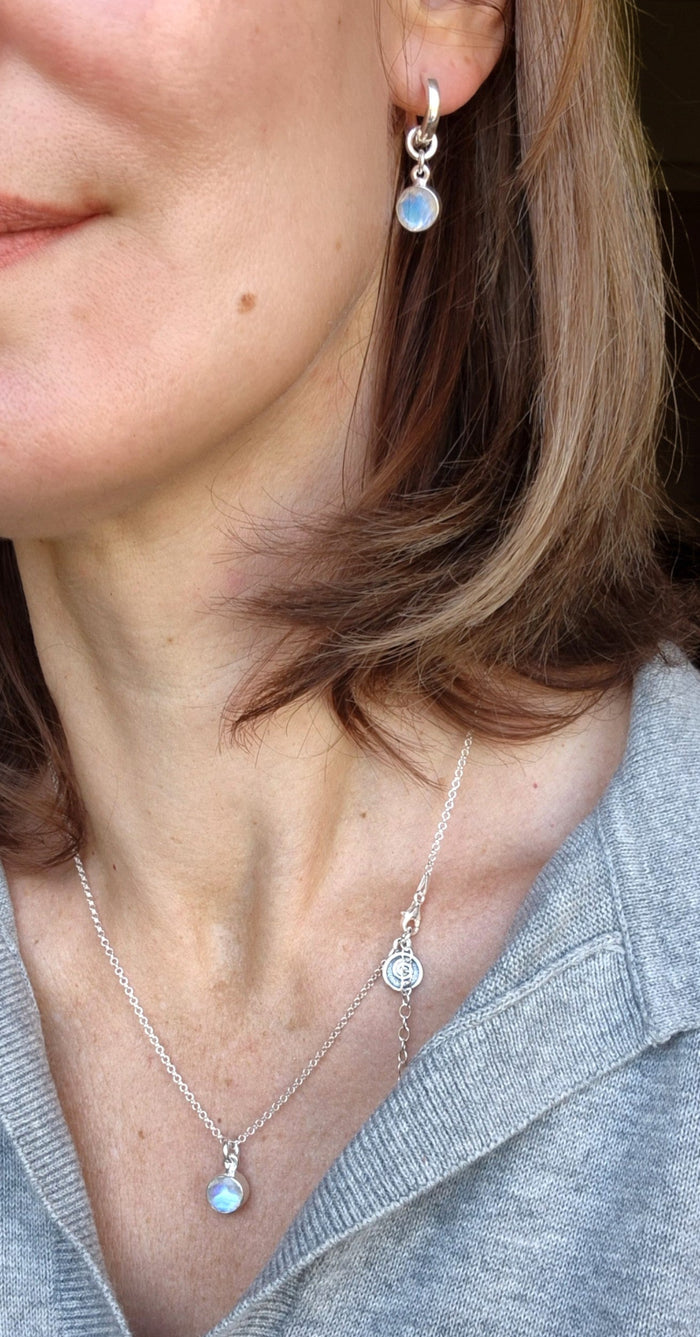 Close-up of a person wearing silver earrings and a necklace with opal stones.