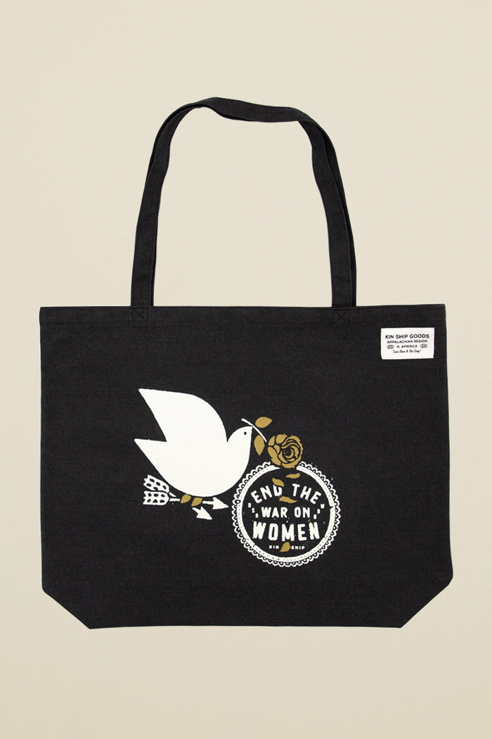 Kin Ship Goods black tote bag with white dove, gold rose, and 'End the War on Women' message in bold black and white circle.