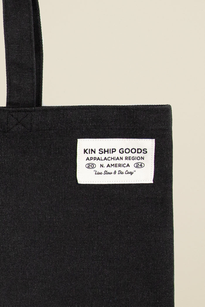 Kin Ship Goods black tote bag with white dove, gold rose, and 'End the War on Women' message in bold black and white circle.