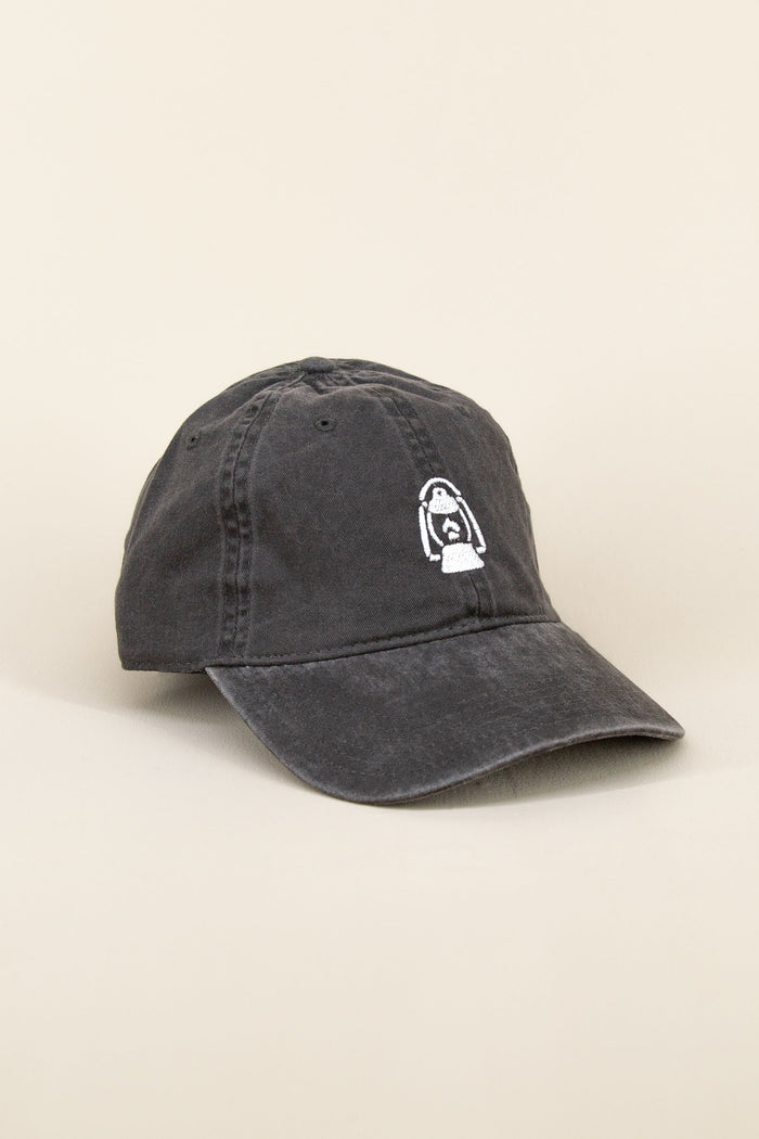 Black Kin Ship Goods baseball cap with white lantern embroidery on front, laid at an angle on neutral background.