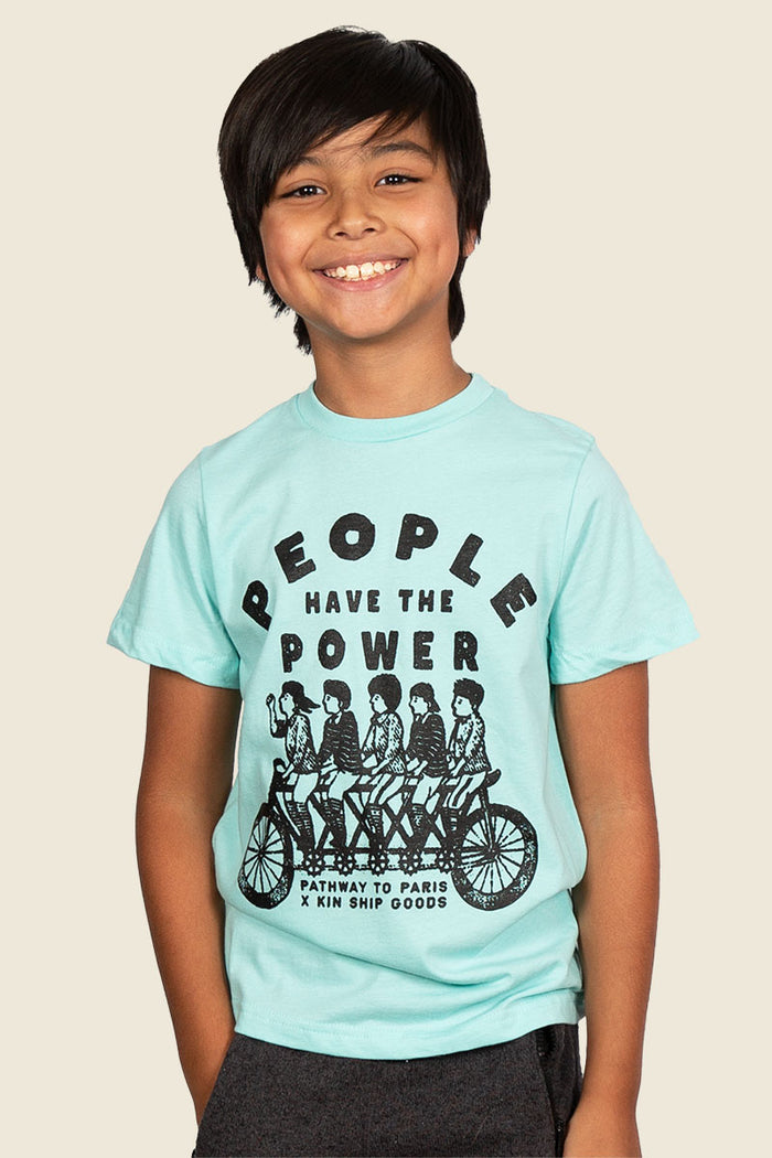 Kin Ship Goods kids tee in aqua with ‘People Have the Power’ tandem bike graphic, a Pathway to Paris collaboration design.