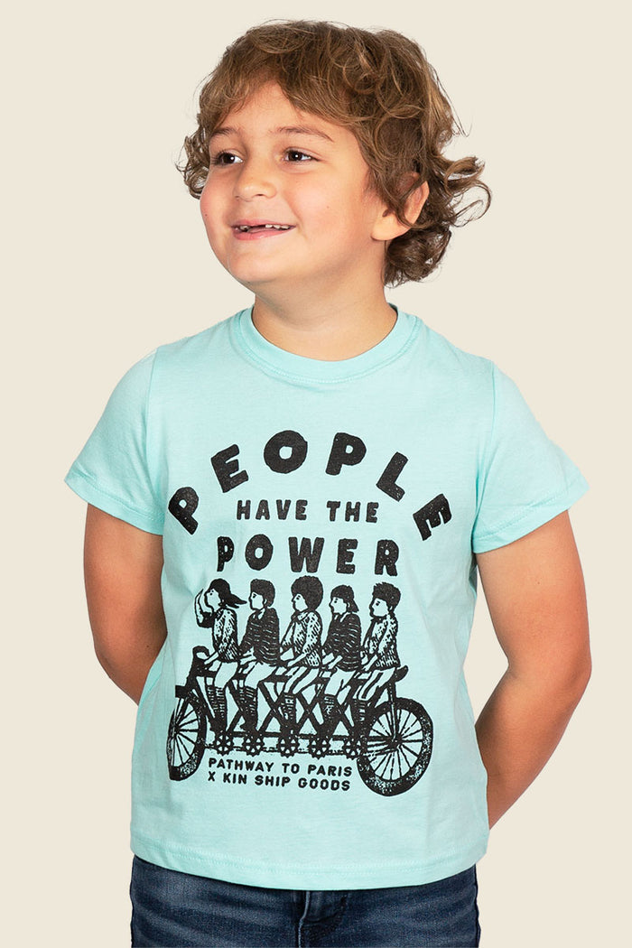 Kin Ship Goods kids tee in aqua with ‘People Have the Power’ tandem bike graphic, a Pathway to Paris collaboration design.