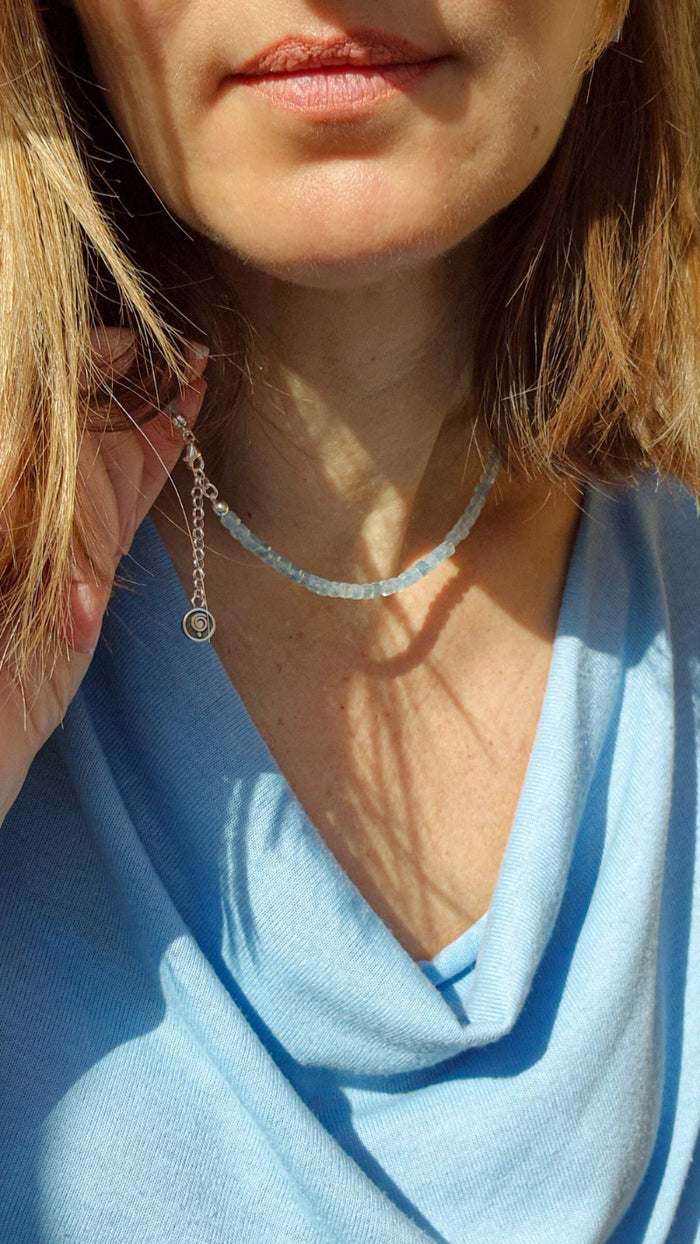 A beaded necklace with light blue aquamarine stones and a handmade silver medallion with a spiral design.