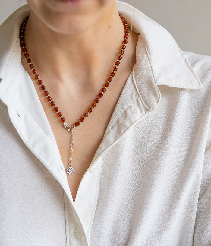 Person wearing a white shirt with a red amber beaded necklace