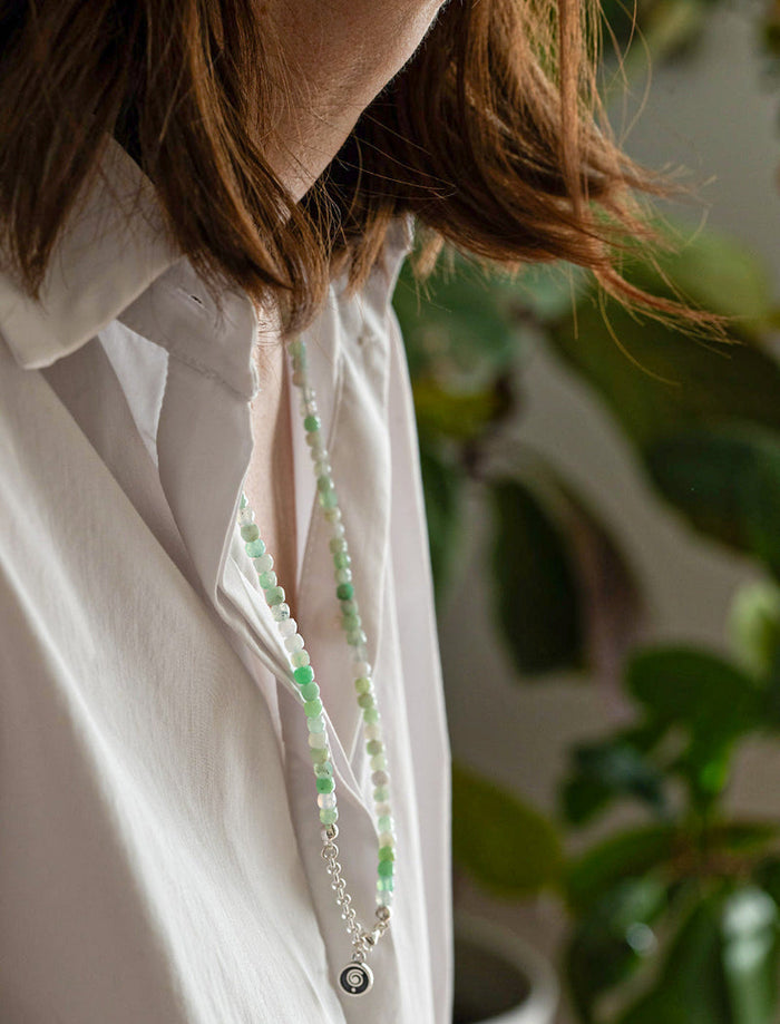 Person wearing a white shirt with a green beaded necklace, blurred background