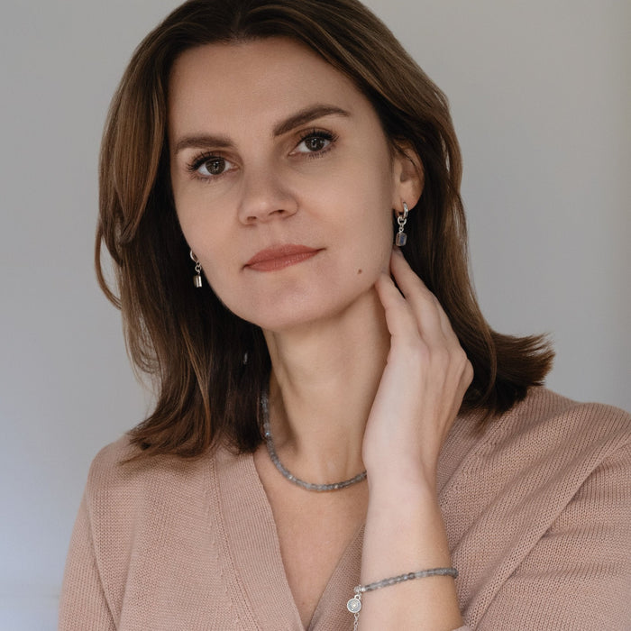 A woman wearing a silver necklace and bracelet with labradorite cube beads.