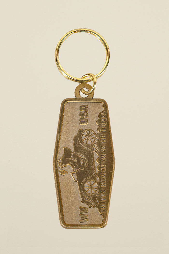 Shitty Roads motel keychain from Kin Ship Goods – vintage-style gold key tag with classic car design. Shitty roads, take me home.
