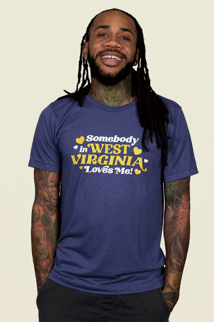Kin Ship Goods adult tee in heather blue with gold and white ‘Somebody in West Virginia Loves Me!’ retro-style graphic.